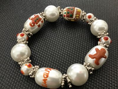 Sale Photo Thumbnail #158: A festive holiday stretch bracelet featuring faux pearl beads accented with painted gingerbread man motifs, a gingerbread house, and text details ("Muffin Man", "Knows"). Separated by silvertone textured spacer beads. Appears to be in good pre-owned condi