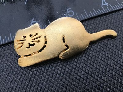 Sale Photo Thumbnail #67: A vintage gold-tone brooch featuring a playful lounging or reclining cat design with openwork facial details and whiskers. Marked 'ULTRA CRAFT ©' on the back. Measures approximately 2.25 inches in length. Standard pin back with rollover safety clasp in g