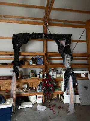 Sale Photo Thumbnail #14: Large wooden arbor structure partially wrapped in black plastic trash bags and white tulle netting inside a workshop. Assorted garage items, artificial floral arrangements, and storage shelves are visible in the background.