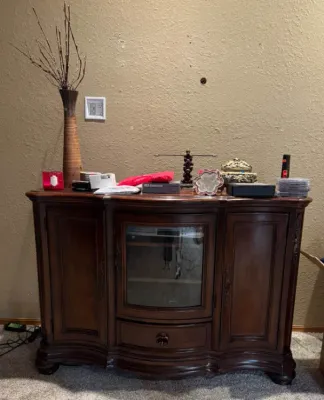Sale Photo Thumbnail #10: Traditional dark wood sideboard media console with a glass-front center cabinet, side panel doors, and various decorative accent pieces displayed on top.