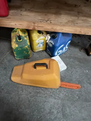 Sale Photo Thumbnail #15: Stihl chainsaw carrying case in orange molded plastic, accompanied by three vintage fuel cans stored beneath a wooden shelf.