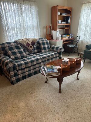 Sale Photo Thumbnail #25: Living room setup featuring a plaid upholstered sofa, an oval wooden Queen Anne style coffee table, and a tall wooden desk hutch in the background.