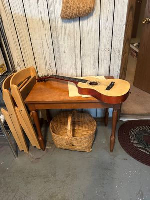 Sale Photo Thumbnail #49: Small acoustic guitar displayed on a wooden side table alongside a woven wicker basket and light wood folding chairs.