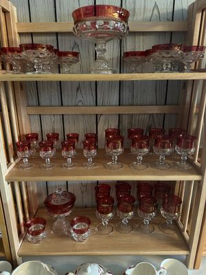 Sale Photo Thumbnail #55: Collection of vintage Kings Crown ruby stain glass stemware, including goblets, sherbet dishes, small cups, and a central pedistaled bowl, displayed on wooden shelves.