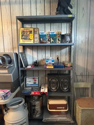 Sale Photo Thumbnail #46: Metal four-shelf utility rack holding vintage sports memorabilia, boxed games, pair of speakers, and a Winnebago personal cooler.