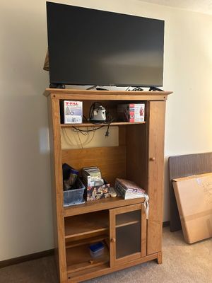 Sale Photo Thumbnail #34: Light oak entertainment center featuring open shelving, a glass-front lower cabinet, and a side door, topped with a flat-screen television.