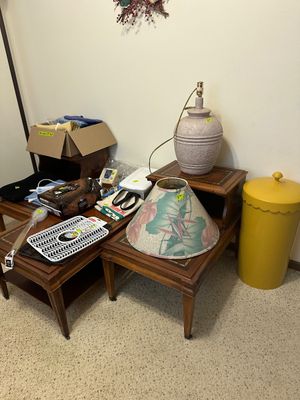 Sale Photo Thumbnail #13: Collection of household goods displaying vintage two-tier wooden end tables, a textured ceramic table lamp with a tropical floral shade, and a yellow cylindrical hamper.