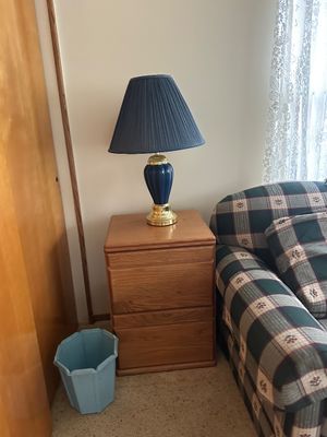 Sale Photo Thumbnail #26: Two-drawer oak nightstand topped with a blue ceramic table lamp featuring a brass base and navy pleated shade.