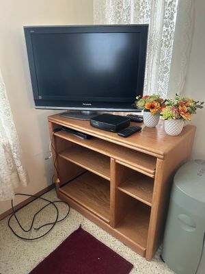 Sale Photo Thumbnail #28: Panasonic flat-screen television sitting atop a light oak media stand with open shelving, accompanied by set-top boxes, remotes, and decorative floral arrangements.