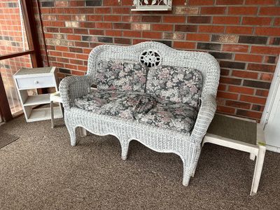 Sale Photo Thumbnail #24: Vintage white painted wicker loveseat with floral cushions, shown alongside small white accent tables.