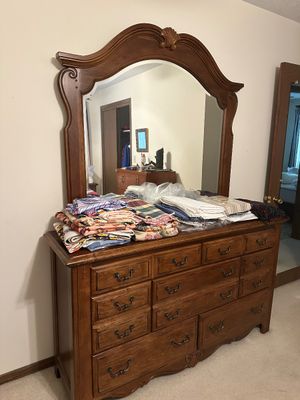 Sale Photo Thumbnail #9: Traditional wooden dresser with attached arched mirror featuring shell carving detail and brass bail handles, stacked with folded linens on top.