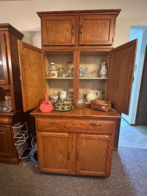 Sale Photo Thumbnail #66: Tall oak hutch with upper and lower cabinet storage, featuring a center shelf filled with glassware, kitchenware, and small decor items.
