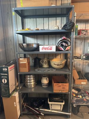 Sale Photo Thumbnail #44: Tall gray metal five-tier storage shelf loaded with various household items, including a Coca-Cola cardboard tray, a motorcycle helmet, stoneware bowls, and tools.