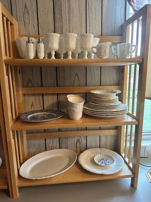 Sale Photo Thumbnail #45: Collection of white glass and ceramic tableware displayed on a light wood three-tier folding bookshelf. Items include milk glass stemware, salt and pepper shakers, teacups, plates, and serving platters.