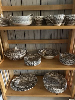 Sale Photo Thumbnail #56: Collection of brown transferware porcelain dishware arranged on light wood shelves, including dinner plates, bowls, teacups, and a covered serving dish with traditional pastoral scenes.
