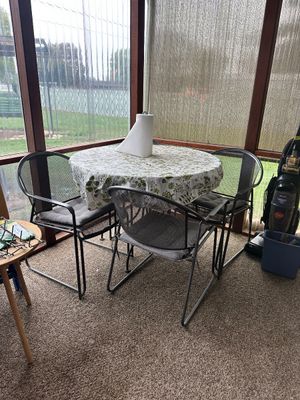Sale Photo Thumbnail #22: Black wrought iron outdoor dining set featuring a round table with a floral tablecloth and three mesh armchairs with grey cushions.