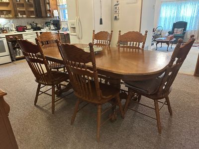 Sale Photo Thumbnail #69: Traditional oak dining set featuring a large oval pedestal table with leaf extension and six matching press-back pressed wood chairs with spindle backs.