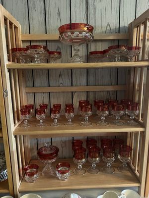 Sale Photo Thumbnail #41: Collection of ruby stained Kings Crown pattern glassware displayed on a wooden shelf unit, including goblets, sherbet cups, a covered candy dish, and a pedestal bowl.