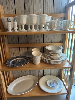 Sale Photo Thumbnail #58: Collection of white milk glass stemware and tableware displayed alongside cream-colored dinnerware and blue-and-white transferware plates on a light wooden shelf.