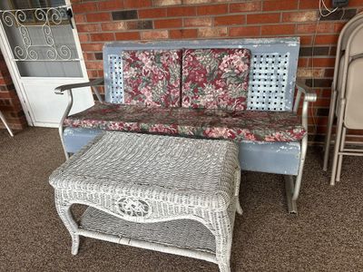 Sale Photo Thumbnail #18: Vintage painted metal patio glider bench with floral cushions paired with a white wicker coffee table featuring a lower shelf.