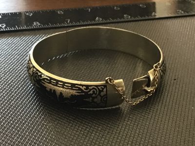 Sale Photo Thumbnail #66: A vintage Siam niello style hinged bangle bracelet featuring black enamel/niello inlay with etched architectural and decorative motifs around the exterior. Equipped with a box tab closure and attached safety chain. Marked 'WHITE ' on the interior. Shows l