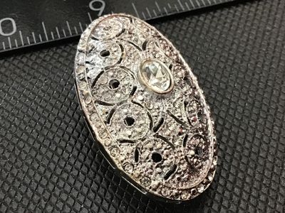 Sale Photo Thumbnail #149: Oval vintage silver-tone brooch featuring an openwork filigree design set with small pavé rhinestones and a central oval crystal. Measures approximately 2 inches wide based on the ruler in photos. Back features a standard pin stem with a rolling c-clasp 