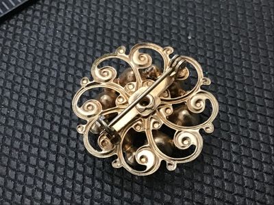 Sale Photo Thumbnail #215: A vintage gold-tone openwork filigree style brooch set with green and clear rhinestones. Features a central large faceted green rhinestone surrounded by clear and smaller green accent stones. Pin back mechanism on reverse. Measures approximately 1 inch in