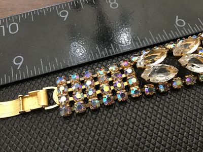 Sale Photo Thumbnail #55: A vintage gold-tone costume jewelry bracelet featuring clear marquise-cut rhinestones flanked by iridescent aurora borealis accent crystals. Features a fold-over clasp closure. Measures approximately 7 inches long. Good vintage condition with light surfac