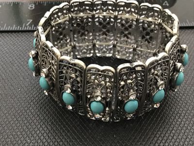 Sale Photo Thumbnail #183: Silver-tone filigree metal stretch bracelet featuring oval turquoise-colored cabochons flanked by clear rhinestones. Features articulated, lattice-style panels strung on elastic cords. Good pre-owned condition with light wear.