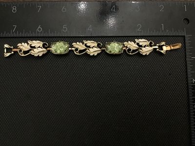 Sale Photo Thumbnail #82: Vintage costume jewelry bracelet by Emmons. Features white painted or enameled metal leaf links interspersed with light green molded glass cabochons set with small clear rhinestones. Signed EMMONS on the foldover clasp. Measures approximately 7 inches in 