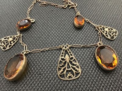 Sale Photo Thumbnail #87: Vintage or antique-style choker necklace featuring intricate metal filigree teardrop charms alternating with bezel-set faceted oval amber/topaz-colored glass stones. Connected on a paperclip-link chain with a hook clasp. Metal shows light tarnishing and p
