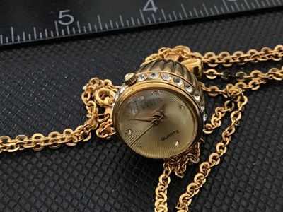 Sale Photo Thumbnail #9: A Joan Rivers Classics quartz pendant watch designed in an acorn shape with clear rhinestone accents around the bezel and a bow-shaped bail. Features a gold-tone sunburst dial with rhinestone hour markers and a matching gold-tone chain. Includes the origi
