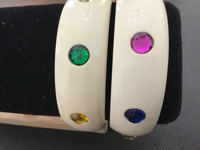 Sale Photo Thumbnail #3: Pair of cream/off-white plastic or lucite thick bangle bracelets studded with round faceted multi-colored rhinestones (red, blue, green, purple, yellow). Each bangle measures approximately 2.5 inches in inner diameter. Both bracelets are in good vintage c