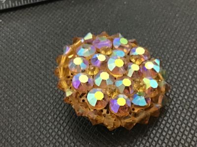 Sale Photo Thumbnail #235: Vintage round domed cluster brooch set with iridescent aurora borealis rhinestones and amber/topaz-colored faceted crystal beads. Features a textured silver-tone backing with a locking pin clasp. Measures approximately 1.5 inches in diameter. In good vint