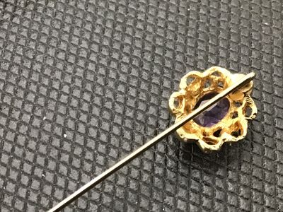 Sale Photo Thumbnail #105: A vintage gold-tone stick pin featuring an openwork filigree setting with an oval faceted purple amethyst-colored stone. Comes complete with a matching gold-tone protective end cap. Total length is approximately 2.5 to 3 inches long based on ruler marking