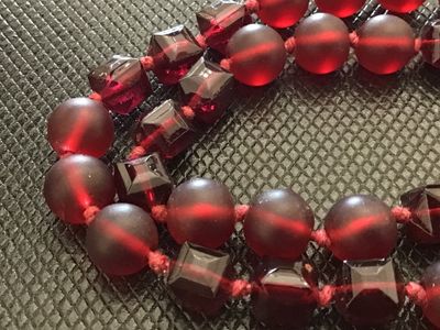 Sale Photo Thumbnail #28: A long single-strand necklace featuring alternating deep red frosted round glass beads and faceted geometric glass beads, hand-knotted on red cord. Finished with a silver-tone lobster clasp closure. Measures approximately 24 to 26 inches in total length. 