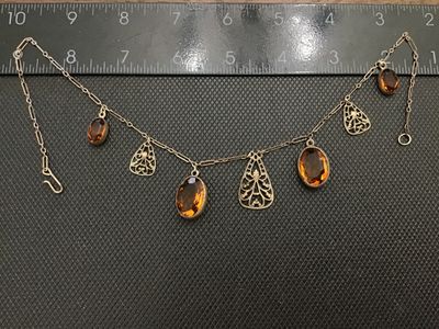 Sale Photo Thumbnail #83: Vintage or antique-style choker necklace featuring intricate metal filigree teardrop charms alternating with bezel-set faceted oval amber/topaz-colored glass stones. Connected on a paperclip-link chain with a hook clasp. Metal shows light tarnishing and p