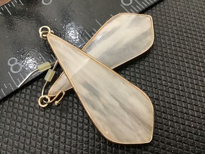 Sale Photo Thumbnail #139: Pair of gold-tone metal dangle drop earrings featuring elongated teardrop-style pendants with semi-translucent white marbled or swirled stone/acrylic inlay. Ear wires include plastic backs. Total length is approximately 2.5 inches. In good pre-owned condi
