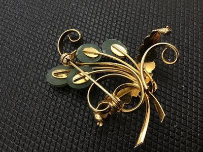 Sale Photo Thumbnail #233: A vintage gold-tone wire-work brooch featuring a leaf and scroll spray design accented with four oval cabochon green stone or glass beads resembling jade. Features textured leaves and a standard pin back clasp. Measures approximately 2 inches long. Good v
