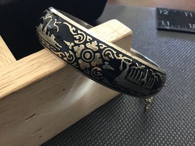 Sale Photo Thumbnail #61: A vintage Siam niello style hinged bangle bracelet featuring black enamel/niello inlay with etched architectural and decorative motifs around the exterior. Equipped with a box tab closure and attached safety chain. Marked 'WHITE ' on the interior. Shows l