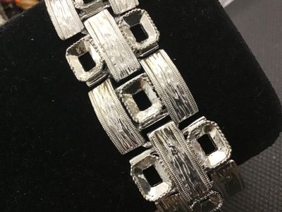 Sale Photo Thumbnail #178: A vintage silver-tone wide link panel bracelet featuring a textured bark-like finish and geometric rectangular cut-out links. Features a fold-over clasp closure. Measures approximately 7.5 inches long. Shows minor vintage wear consistent with age, but ove