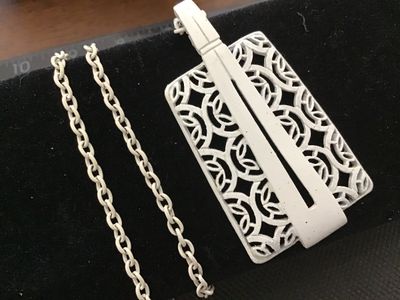 Sale Photo Thumbnail #90: A vintage mid-century style white enamel pendant necklace featuring an openwork, filigree geometric lattice pattern with a sleek modern overlay accent. Suspended from a matching white enamelled link chain with a gold-tone spring ring clasp. 

- Pendant Di