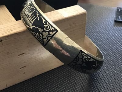 Sale Photo Thumbnail #64: A vintage Siam niello style hinged bangle bracelet featuring black enamel/niello inlay with etched architectural and decorative motifs around the exterior. Equipped with a box tab closure and attached safety chain. Marked 'WHITE ' on the interior. Shows l