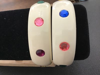 Sale Photo Thumbnail #2: Pair of cream/off-white plastic or lucite thick bangle bracelets studded with round faceted multi-colored rhinestones (red, blue, green, purple, yellow). Each bangle measures approximately 2.5 inches in inner diameter. Both bracelets are in good vintage c