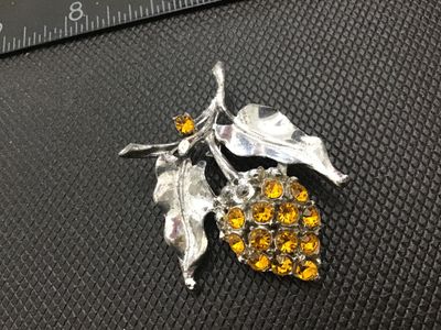 Sale Photo Thumbnail #176: A vintage silver-tone metal brooch featuring a pinecone design accented with bright amber-colored rhinestones and detailed leaves. The pin mechanism on the back includes a standard rollover safety clasp. Shows light vintage wear and tarnish on the reverse