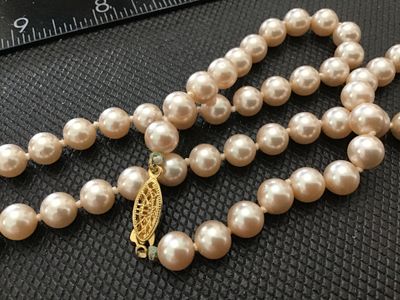 Sale Photo Thumbnail #158: Single strand pearl necklace featuring cream/pinkish tone beads and a gold-tone filigree fishhook clasp. Individually knotted between pearls. Appears to be vintage. Shows light wear consistent with age, with minor oxidation near the clasp connection point