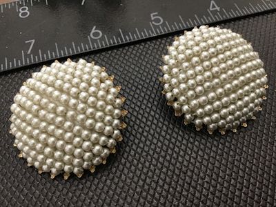 Sale Photo Thumbnail #106: Pair of vintage round clip-on earrings featuring clustered white faux pearl beads in a domed pattern. Set in a gold-tone filigree metal backing. Each earring measures approximately 1.25 inches in diameter. Good vintage condition with light, age-appropriat