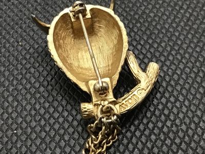 Sale Photo Thumbnail #195: A vintage gold-tone owl brooch by Avon featuring red rhinestone eyes and dangling chain accents from the branch perch. Marked 'Avon ©' on the back. Includes a standard rollover safety clasp pin back. In good vintage condition with minor surface wear cons