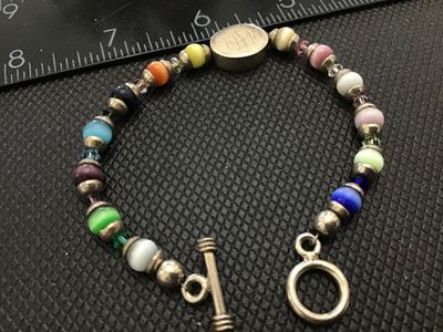 Sale Photo Thumbnail #211: A beaded toggle-clasp bracelet featuring colorful cat's eye synthetic or glass beads alternating with faceted crystal spacers and silver-tone accents. Includes an oval central charm with an engraved script monogram ("MJL"). The toggle ring is stamped "925
