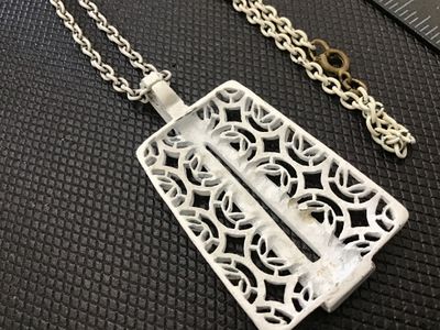 Sale Photo Thumbnail #92: A vintage mid-century style white enamel pendant necklace featuring an openwork, filigree geometric lattice pattern with a sleek modern overlay accent. Suspended from a matching white enamelled link chain with a gold-tone spring ring clasp. 

- Pendant Di
